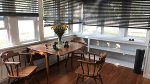 Un comedor con una mesa y sillas de madera, un jarrón con flores y una ventana con persianas.