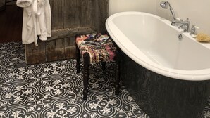 Un baño con puerta de madera, una bañera blanca y baldosas de suelo estampadas.