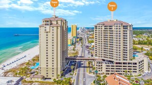 Zwei hohe Hotels mit Balkonen, ein Strand und ein Steg im Hintergrund.