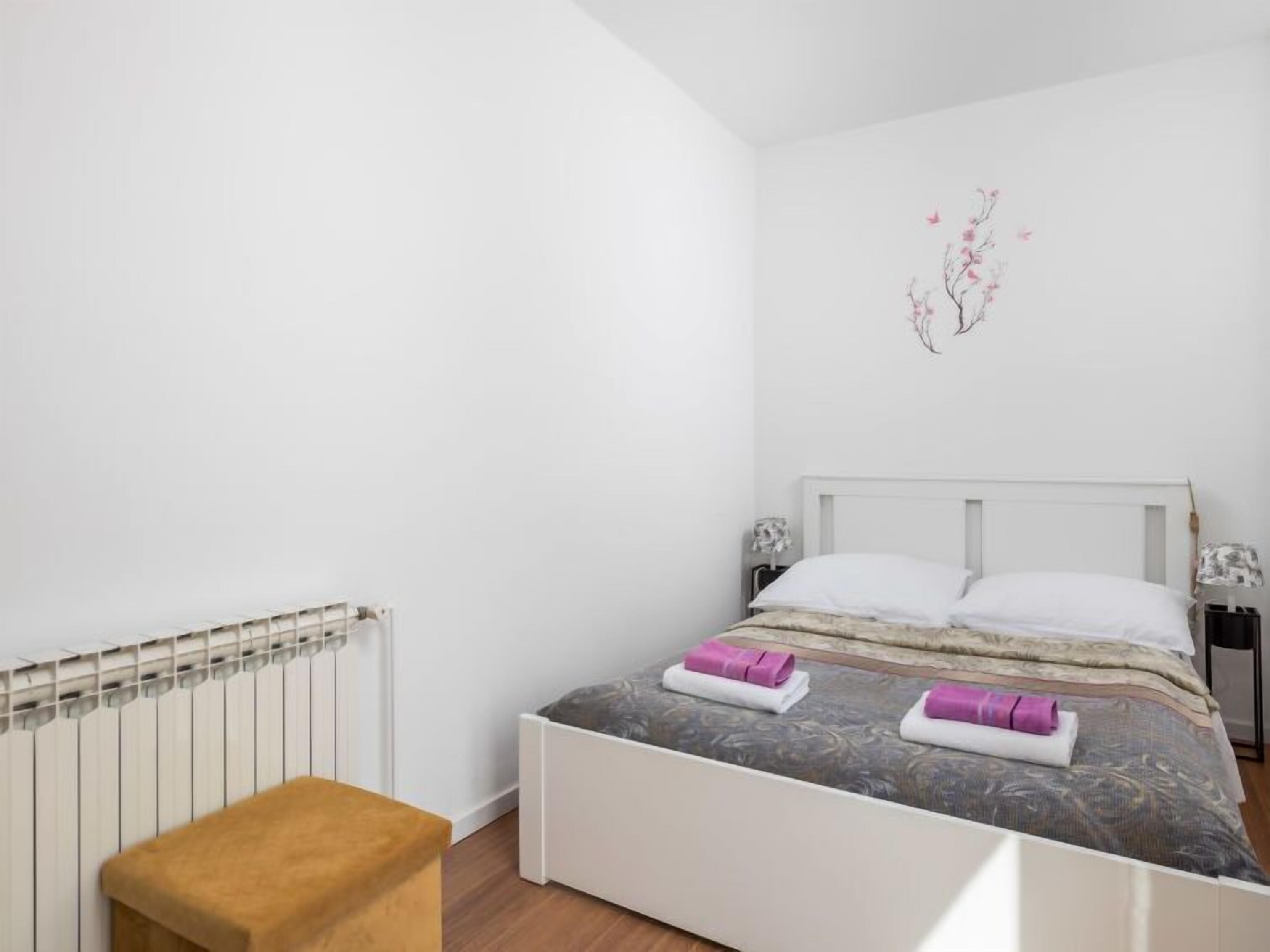 Una camera da letto con un letto bianco, una panca di legno, un termosifone e una decorazione a parete.