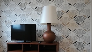 A TV on a wooden stand with a remote control, a brown lamp, and a patterned wallpaper. - North Star Flats @dom Luís I Bridge (Vila Nova de Gaia)