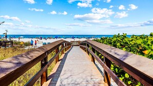 A wooden boardwalk leading to a beach with umbrellas and people. - Best View on Marco Island, #909 @ the Apollo (Marco Island)