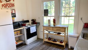 A compact kitchen with a refrigerator, microwave, stove, and wooden shelves. - Grey Wolf Family Style Cottage on Wolf Lake Waterfront (Grass Lake)