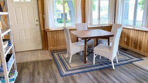 A room with a wooden floor, a white door, a window with curtains, a table with chairs, and a bookshelf. - Grey Wolf Family Style Cottage on Wolf Lake Waterfront (Grass Lake)