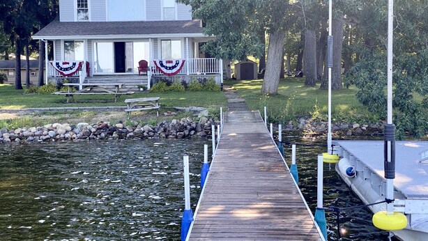 A house with a dock extending into a body of water, surrounded by trees and a grassy area. - Grey Wolf Family Style Cottage on Wolf Lake Waterfront (Grass Lake)