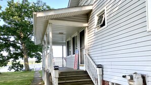 A two-story house with a front porch, a welcome sign, and a view of a lake. - Grey Wolf Family Style Cottage on Wolf Lake Waterfront (Grass Lake)