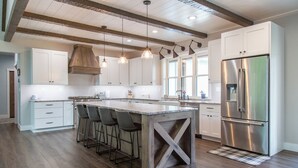 Una cocina moderna con armarios blancos, un refrigerador de acero inoxidable, una isla de madera con taburetes y luces colgantes.