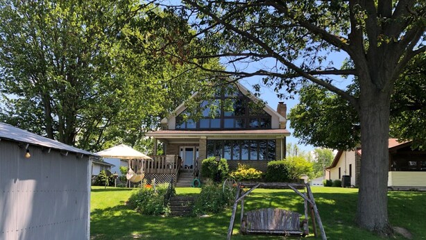 Ein zweistöckiges Haus mit Veranda, Schaukel und kleiner Gartenlaube.