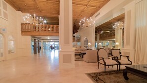 Un hall d’entrée spacieux avec un plafond haut, des lustres, un coin salon avec des fauteuils et un grand miroir qui reflète l’espace.