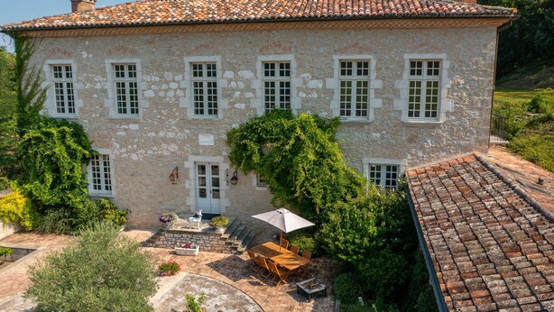 Un edificio in pietra con tetto in tegole, un patio con tavolo e sedie e un’area giardino.