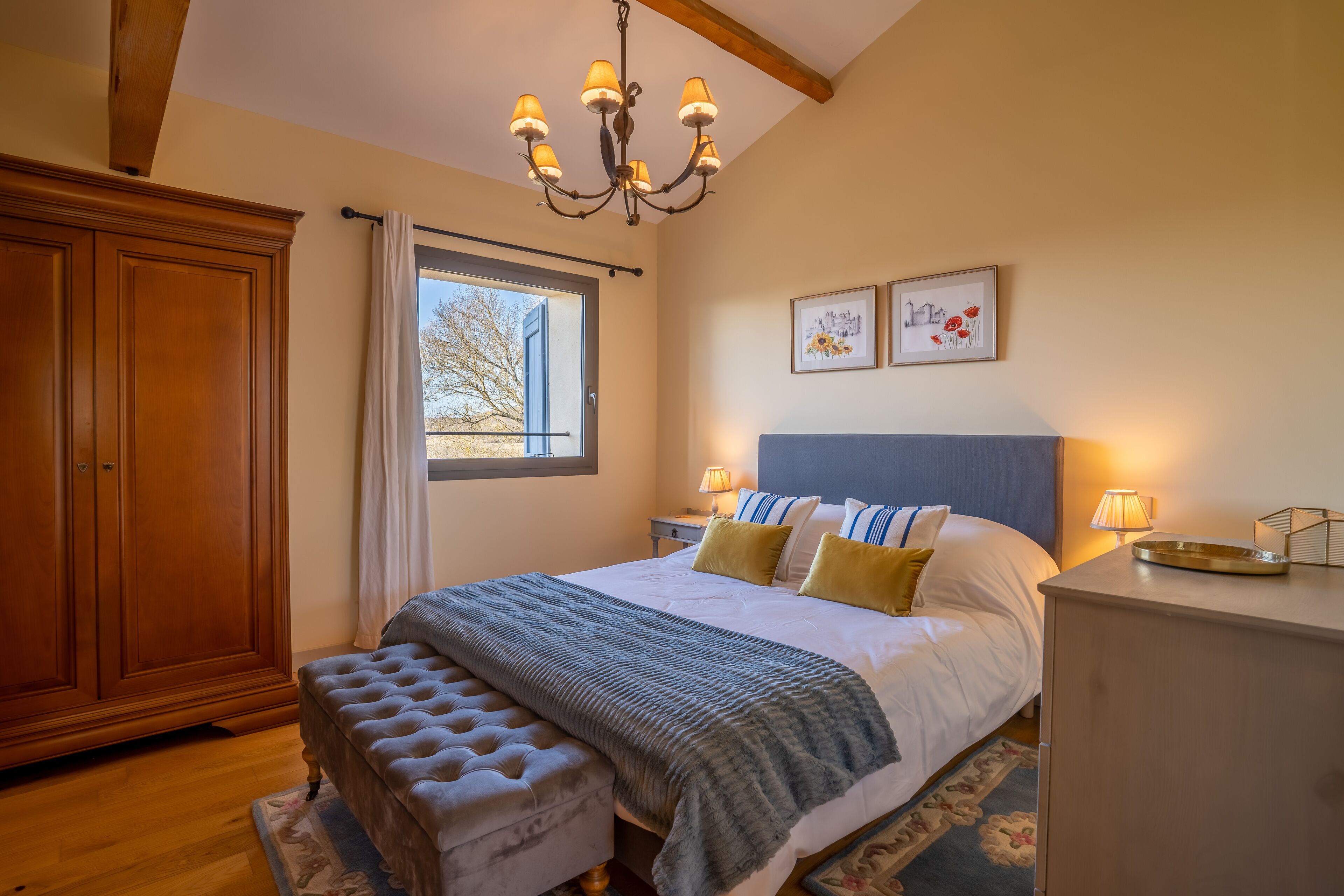 Une chambre à coucher avec un grand lit, une armoire en bois, un lustre et une fenêtre avec des rideaux.
