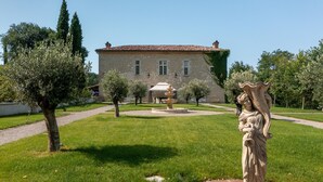 Un edificio in pietra con tetto a tegole, una fontana al centro e una statua in un giardino curato.