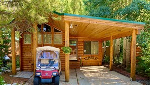 Una cabaña de madera con un porche cubierto, un carro de golf rojo y un letrero que dice 'Welcome'.
