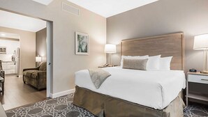 A hotel room with a large bed, a bedside table with a lamp, a chair, and a view of the kitchen area. - Charleston 1BR Deluxe Prime King Street property (Charleston)