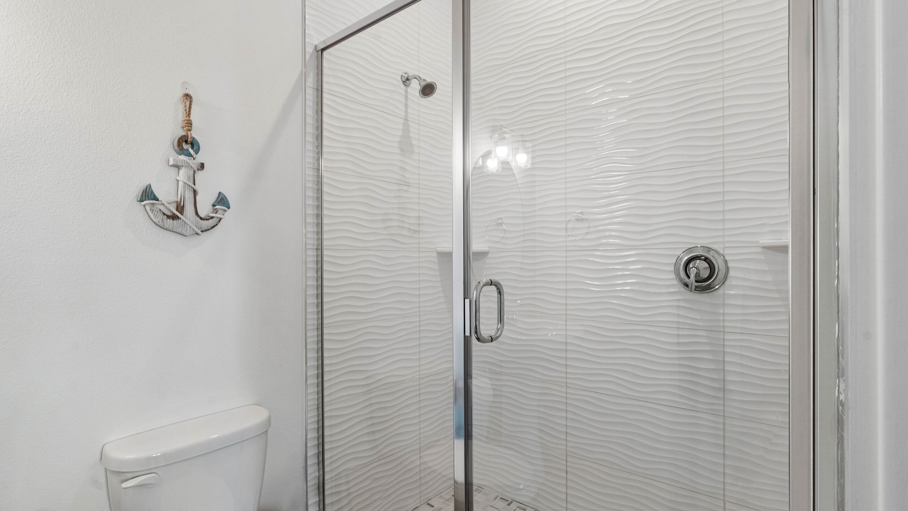 Casa de banho com cabine de duche em vidro, sanita e um porta-toalhas com uma toalha e um objeto decorativo pequeno.