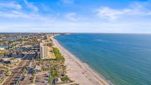 An aerial view of a coastal city with a wide beach, clear blue sky, and a mix of residential and commercial buildings along the shoreline.