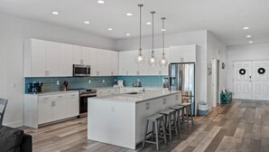 A modern kitchen with white cabinetry, a central island with stools, stainless steel appliances, and a teal backsplash.