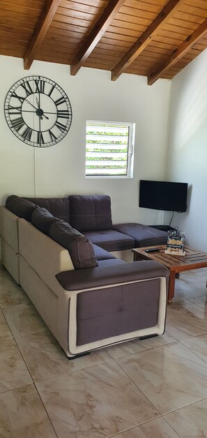 Relax in this inviting living room with a sofa, flat-screen TV, and a coffee table, offering a view of lush greenery.