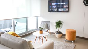A modern living room with a sofa, a round coffee table, a grey armchair, a potted plant, and a flat-screen TV mounted on the wall displaying various streaming services. - Cozy Studio Perfect to Home Office or Relax (San José)