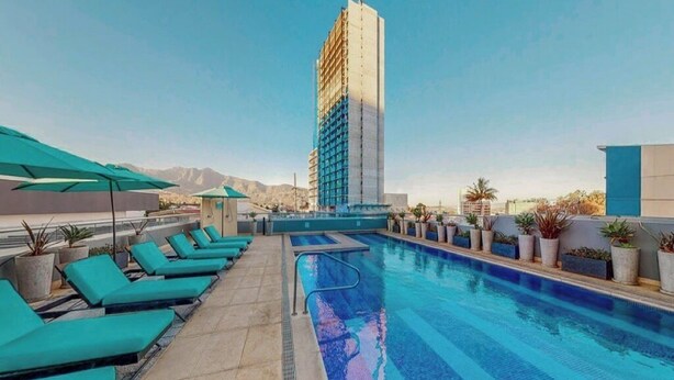 A rooftop pool with lounge chairs and potted plants, surrounded by a modern building. - Cozy Studio Perfect to Home Office or Relax (San José)