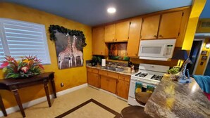 A kitchen with wooden cabinets, a gas stove, a microwave, and a dining area with a table and chairs. - Bakersfield Safari Retreat (Bakersfield)