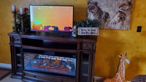 A fireplace with a TV on top, a sign saying "We're So Glad You're Here", and a giraffe statue. - Bakersfield Safari Retreat (Bakersfield)