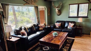 A cozy living room with a black leather sofa, a wooden coffee table, and a mounted deer head on the wall.