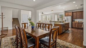 Un comedor amplio con una mesa y sillas de madera, una cocina con armarios de madera y una escalera que conduce a otro nivel.