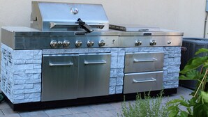 Cocina exterior de acero inoxidable con una parrilla empotrada, varios hornos y un frente de piedra.