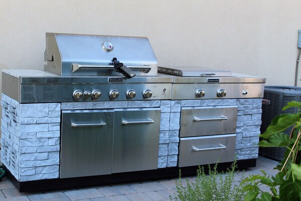 Cocina exterior de acero inoxidable con una parrilla empotrada, varios hornos y un frente de piedra.