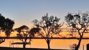 Sonnenuntergang mit Silhouette von Bäumen und einem Gebäude über dem Wasser.