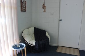 A corner room with a white door, a small round table with a blue mat, a white chair with a black blanket, and a wall decoration of a fish.