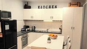 Una cucina moderna con mobili bianchi, un frigorifero nero, un forno a microonde e un tavolo da pranzo con sedie.