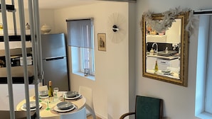 A dining area with a table set for four, a chair, a decorative mirror, and a view of a kitchen through a window. - House (Wintzenheim)