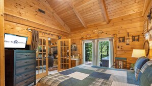 Ein Schlafzimmer in einer Holzhütte mit Bett, Schminktisch und einem Fernseher, der RENTBR anzeigt.