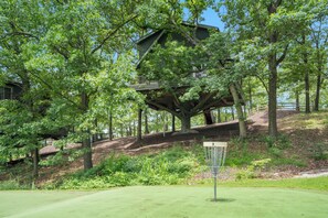 Une cabane perchée dans les arbres, construite à l’intérieur d’un grand arbre, entourée d’une végétation luxuriante et donnant sur un terrain de golf.