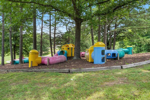 A playground with colorful slides and play structures surrounded by trees. - Rustic Log Cabin Near Thunder Ridge w Private Hot Tub & Free Attraction Tickets_Community Amenities! (Ridgedale)