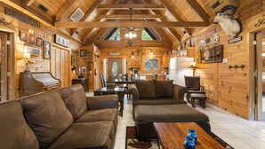 Ein gemütliches Blockhaus-Interieur mit Holzwänden, einem Klavier, Ledersofas und einem Essbereich.