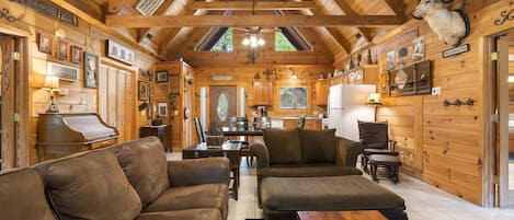 A cozy cabin interior with wooden walls, a piano, leather sofas, and a dining area.
