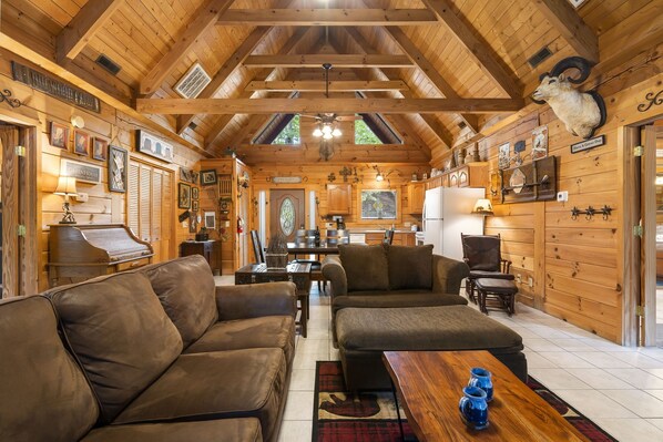 Un intérieur de chalet chaleureux avec des murs en bois, un piano, des canapés en cuir et un coin repas.