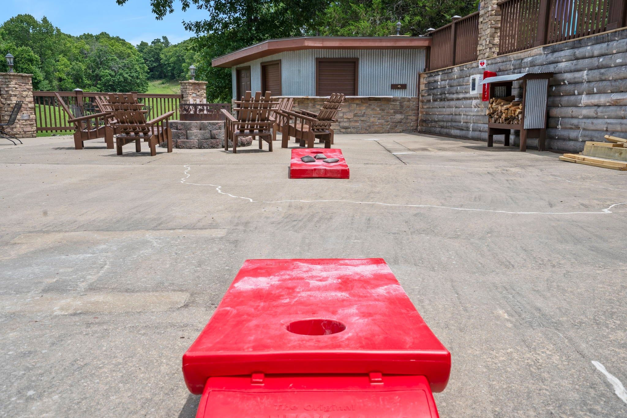 Una cabaña de troncos con mobiliario exterior, un brasero rojo y un muro de piedra.