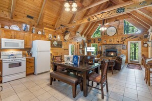 L’intérieur d’un chalet rustique, avec des murs en bois, une cheminée en pierre, un coin repas et une cuisine équipée d’appareils électroménagers modernes.