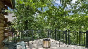 A wooden deck with metal chairs and a metal table, surrounded by a black metal fence, overlooking a wooded area. - Rustic Log Cabin Near Thunder Ridge w Private Hot Tub & Free Attraction Tickets_Community Amenities! (Ridgedale)