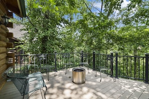 A wooden deck with metal chairs and a metal table, surrounded by a black metal fence, overlooking a wooded area. - Rustic Log Cabin Near Thunder Ridge w Private Hot Tub & Free Attraction Tickets_Community Amenities! (Ridgedale)