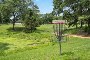 Un panier de disc golf avec un panneau indicateur, entouré d’un champ herbeux bordé d’arbres.