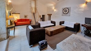 A spacious living area with a high ceiling, a staircase, and a mix of seating options including a red sofa, two white sofas, and a brown wicker sofa.
