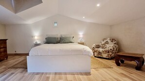 A bedroom with a large bed, a wooden dresser, a patterned armchair, and a small table.