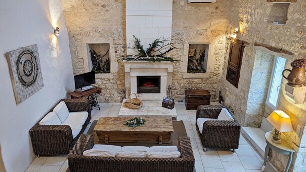 A cozy, stone-walled living room with a fireplace, wicker furniture, and holiday decorations.