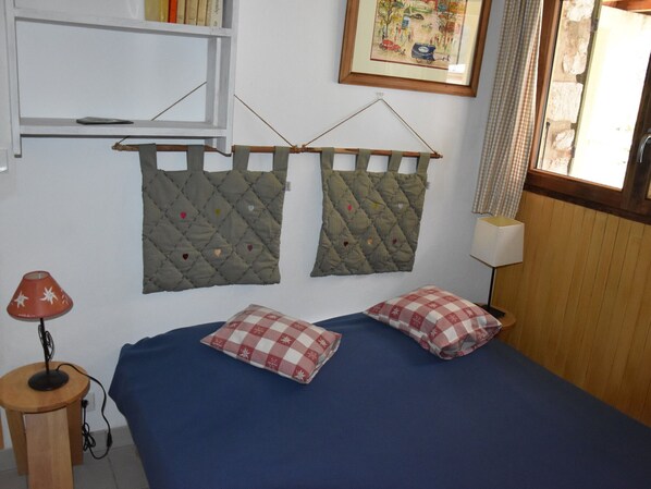 A bedroom with a blue bed, two quilts with heart patterns, a red lamp, and a framed picture on the wall.