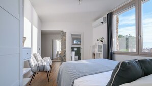 A modern bedroom with a large bed, a seating area with chairs, a stone accent wall, and a view of the outdoors. - Casa Frontemare con Scesa al Mare Privata (Castiglioncello (LI))